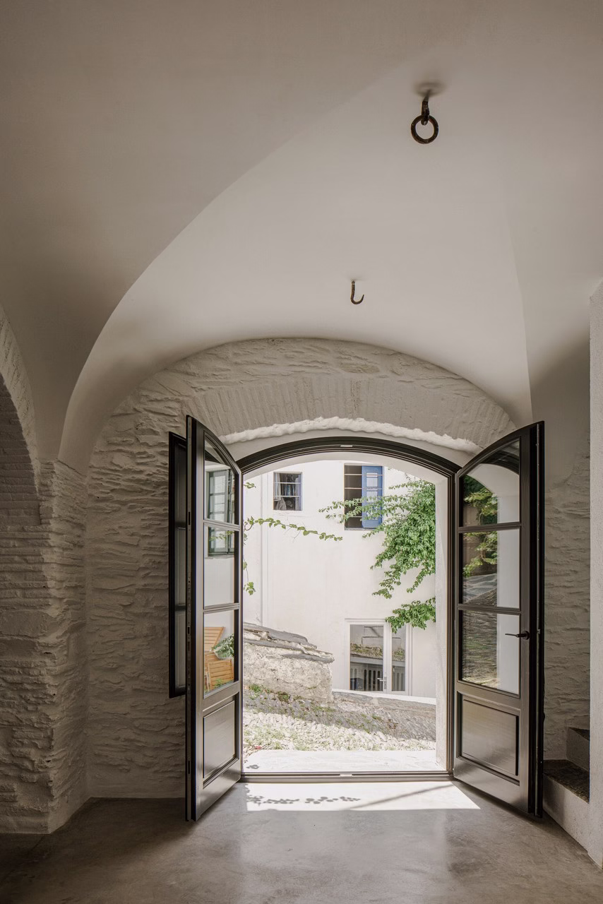 Arched stone entrance with open double doors to sunlit courtyard.