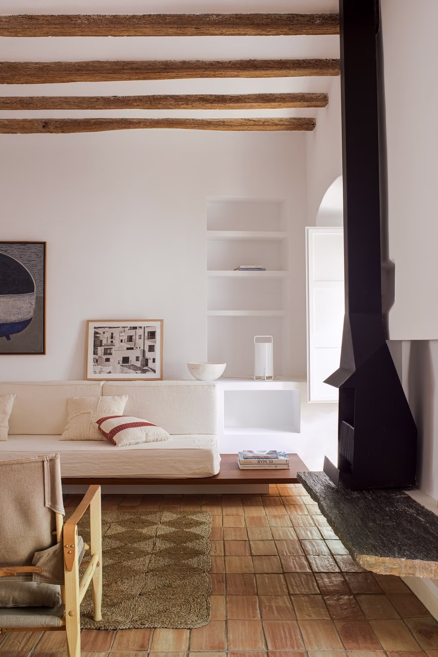 Rustykalne wnętrze z białą kanapą, drewnianymi belkami i glinianą podłogą.